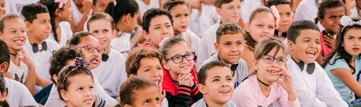 Foto de crianças sorridentes entre 6 e 8 anos atentas a apresentação do Concerto Didático Brasil de Tuhu.